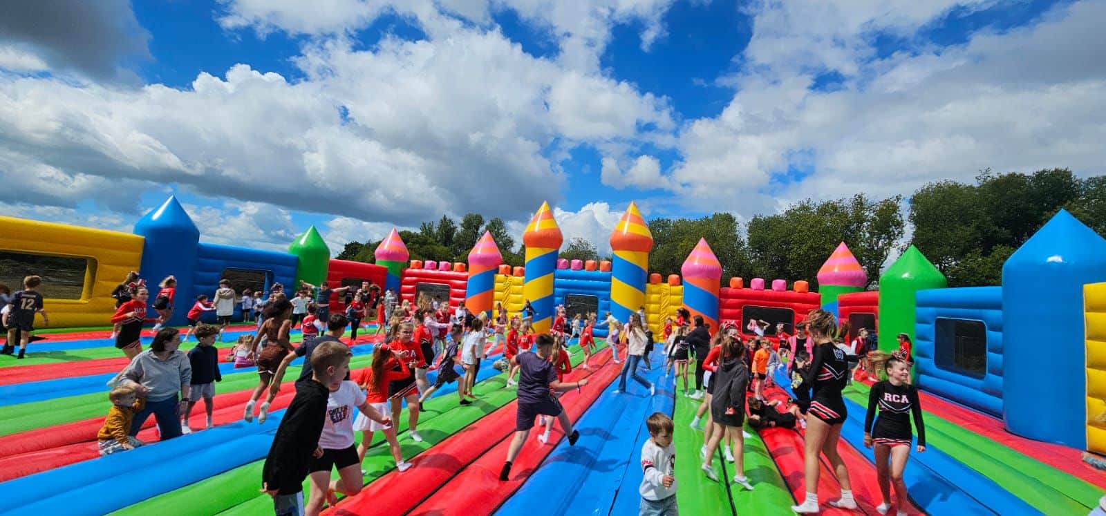 BouncyCastle Children playing on a large, colorful bouncy castle under a partly cloudy sky.