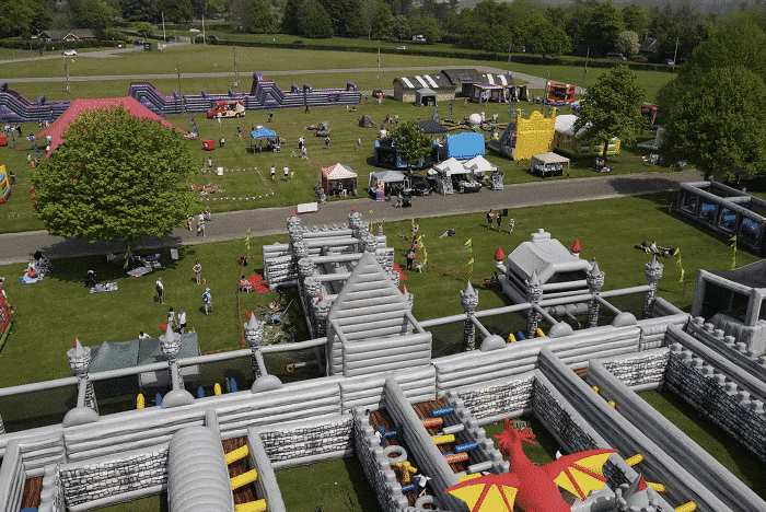 Castle-FamilyFest Aerial view of a park with an inflatable castle maze, people, and festival booths.
