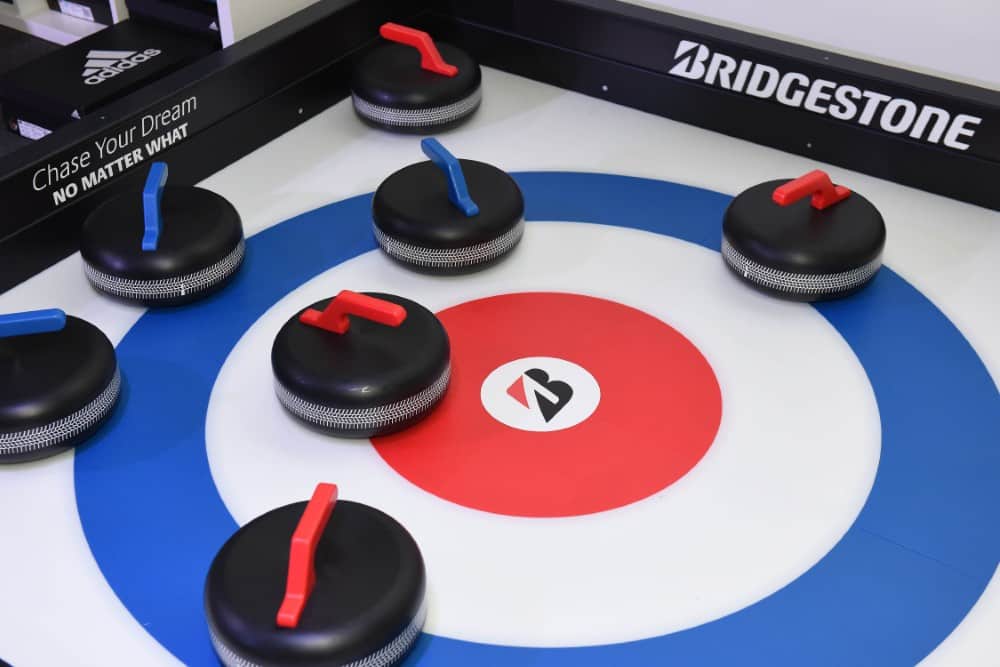 CurlingCloseUp Close-up of curling stones with red and blue handles on a curling target with sponsor logos.
