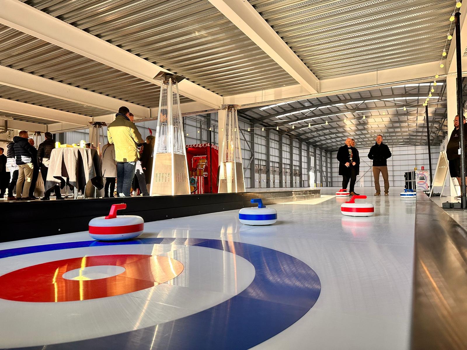 CurlingGame People play curling indoors with several curling stones on the ice.