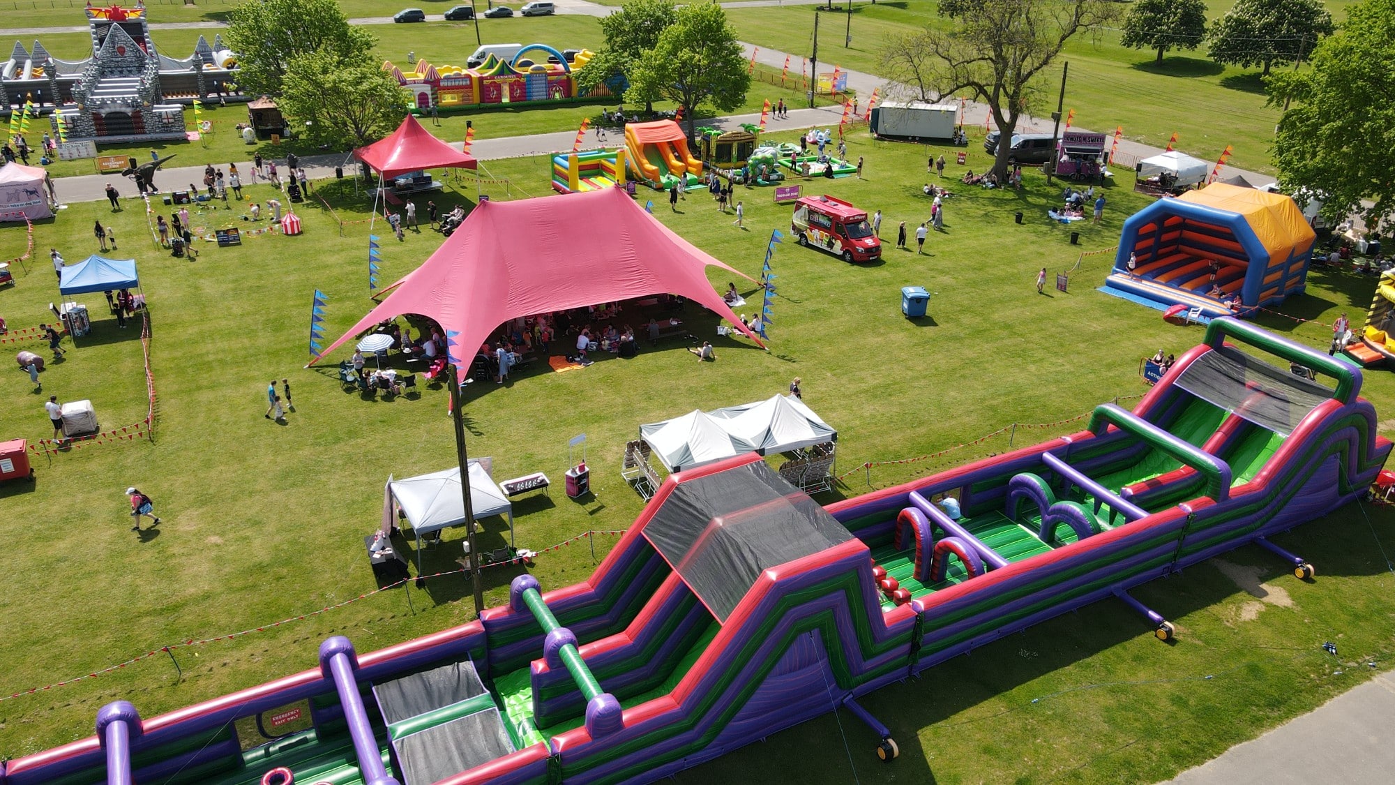 default A park festival with tents, bounce houses, food trucks, and people enjoying outdoor activities.