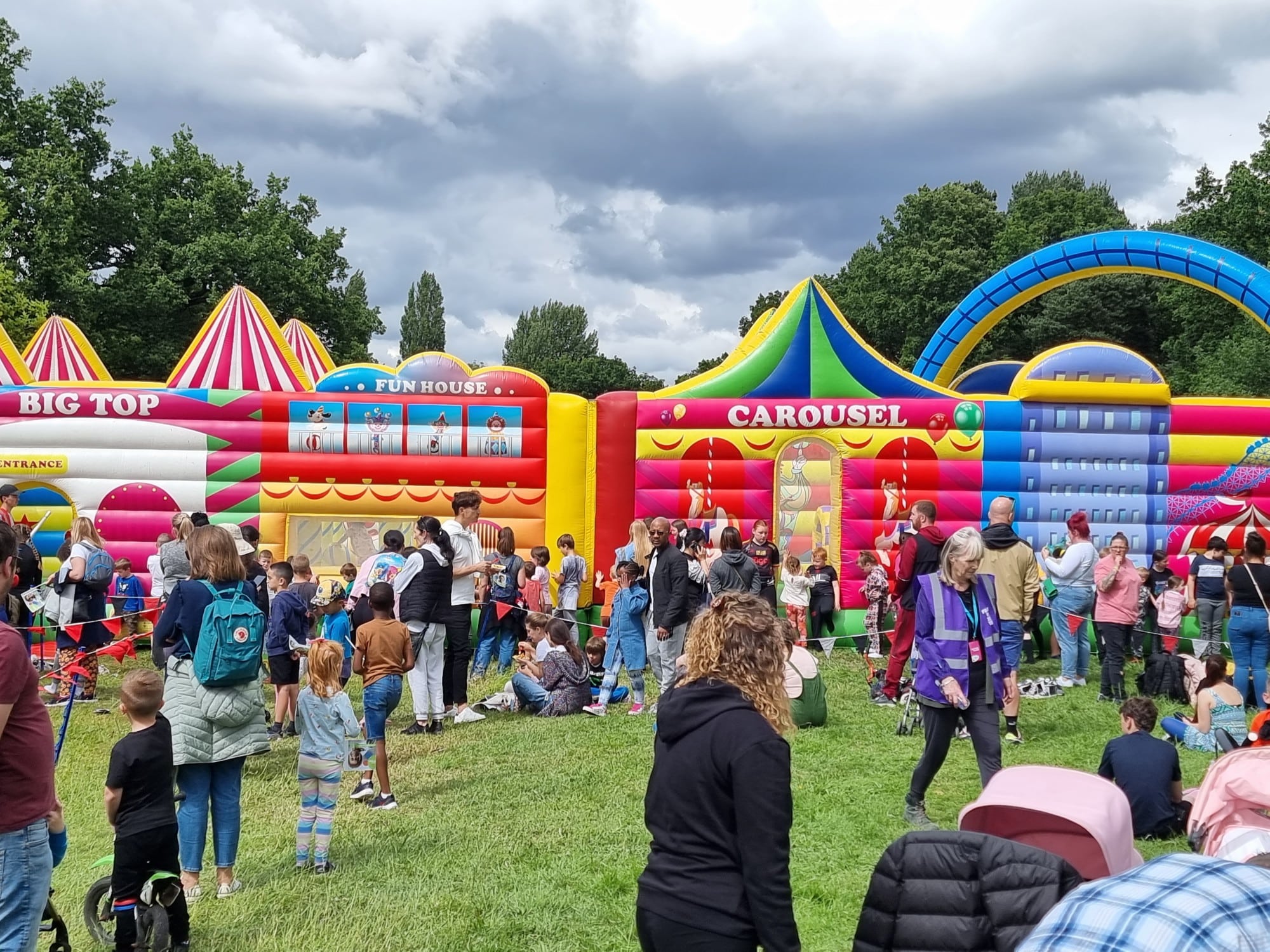 Fun Fair Park Crowd of people and children at a fun fair with colorful inflatable attractions in a park.