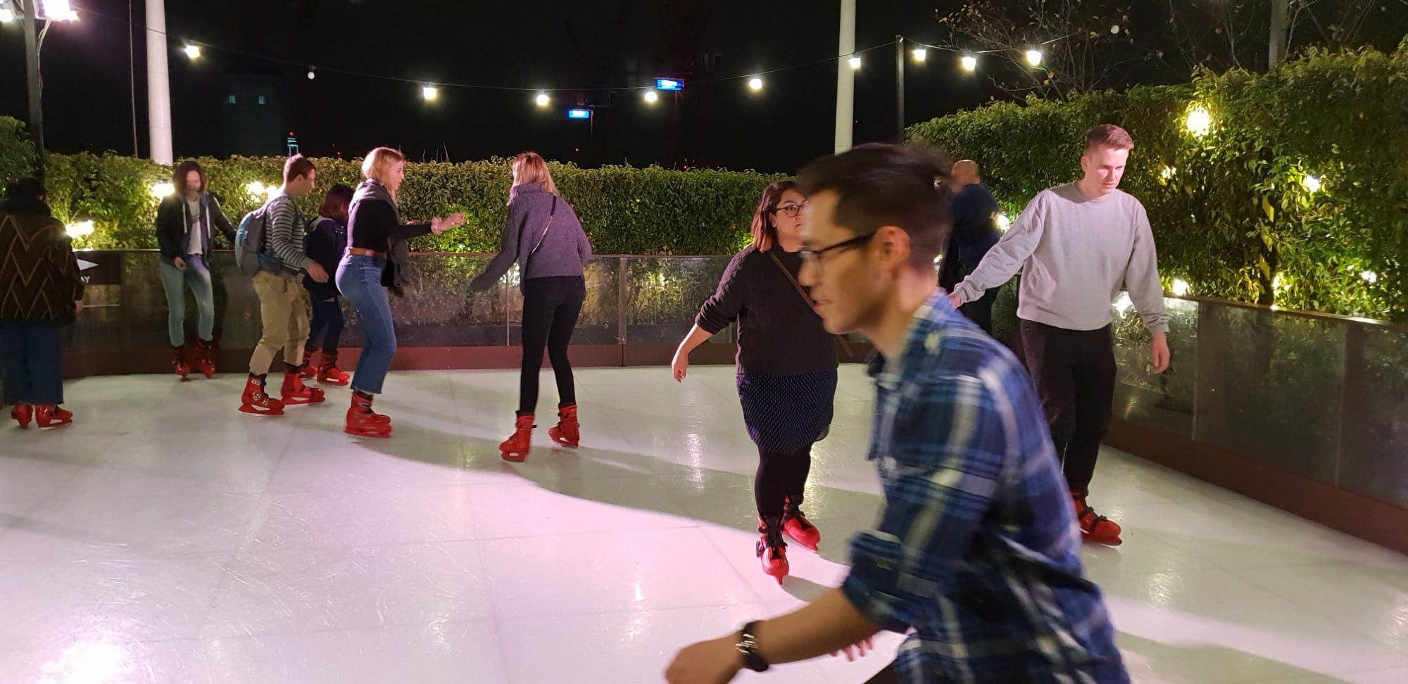 People ice skating outdoors at night under string lights.