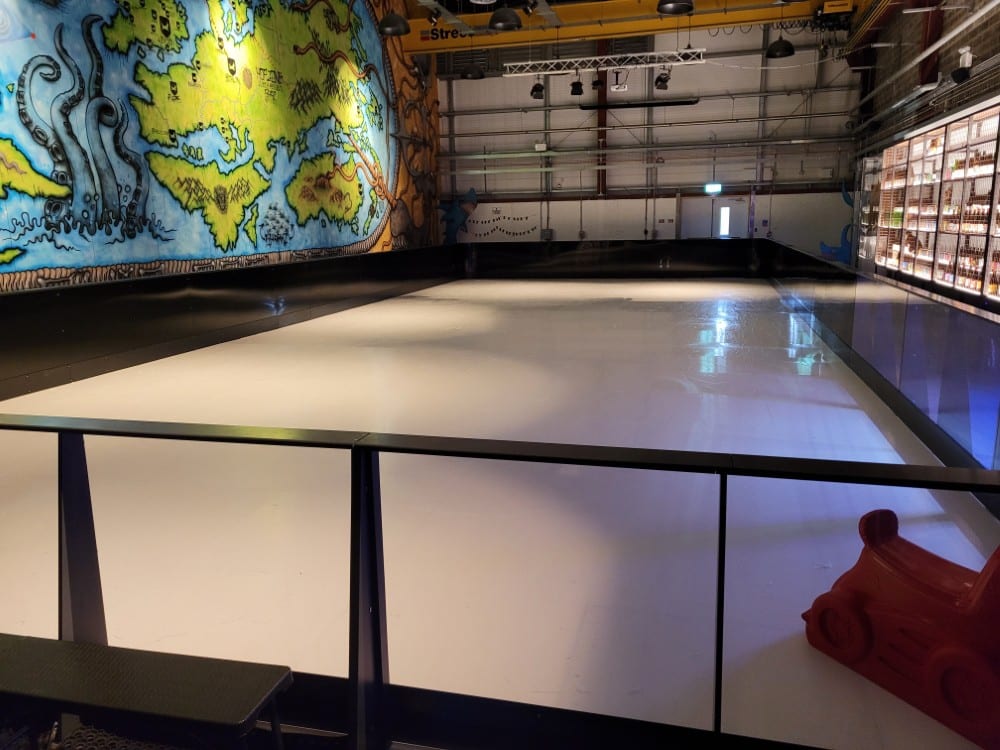 Indoor ice rink with a colorful mural on the wall and a red skating aid in the corner.