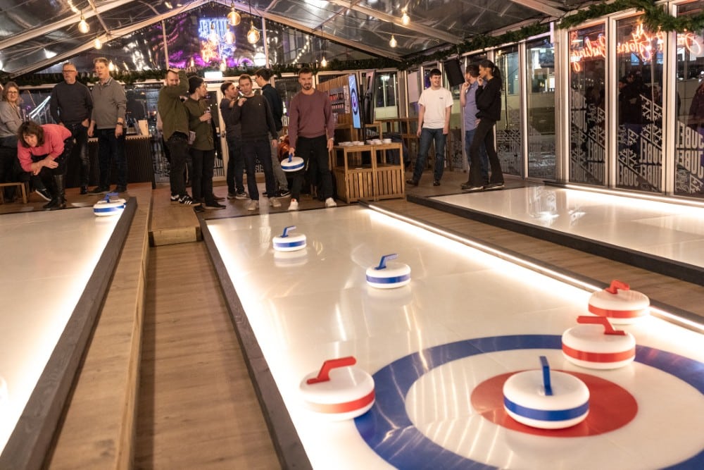 LondonCurlingPopUp People play indoor curling on illuminated lanes at a pop-up venue in London.