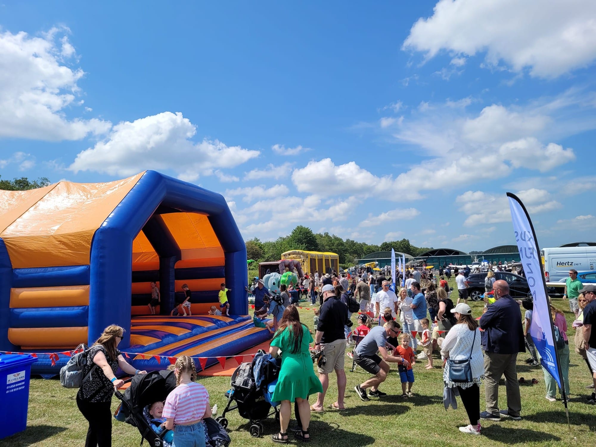 Mega Fun Fest 2 Crowd of people at an outdoor festival, with a large inflatable bounce house under a sunny sky.