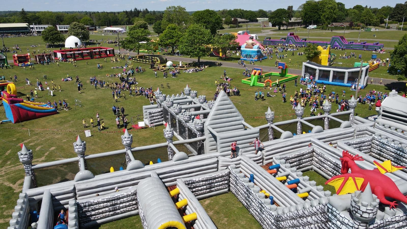 MegaFamilyFunFest-Castle Aerial view of a large outdoor event with inflatable castles, slides, and many people on a grassy field.