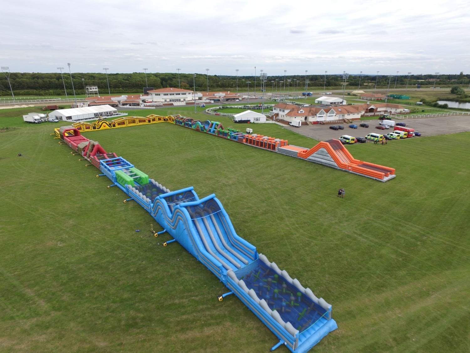 Sidemen-Labyrinth A large inflatable obstacle course is set up on a grassy field near buildings and parked cars.
