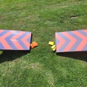Two cornhole boards with orange and yellow bean bags on grass.