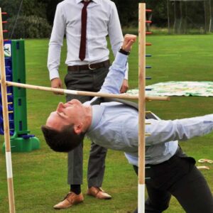 A man in business attire plays limbo outdoors on a grassy lawn.