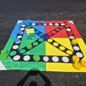 Giant Ludo board with large colorful pieces and a big yellow die on the ground.