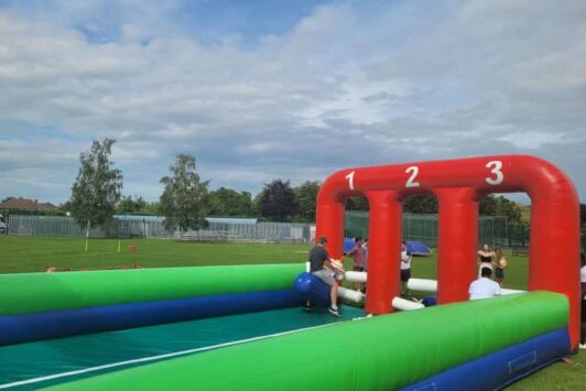 People racing on inflatable horses on an outdoor inflatable track with numbered lanes.