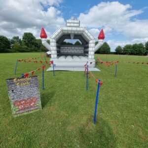 Medieval-themed bouncy castle set up in a field, surrounded by red tape and a safety sign.