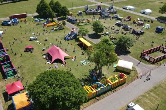 Aerial view of a large outdoor family festival with inflatable attractions and people on a grassy field.