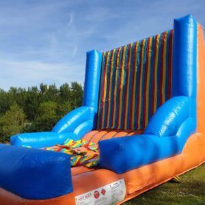 Inflatable Velcro wall game with bright stripes and a velcro suit lying on top, set outdoors.