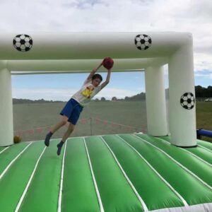 A child jumps to catch a ball on an inflatable soccer game outdoors.