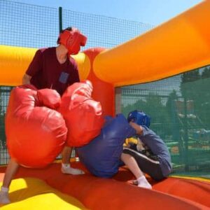 Two people boxing in an inflatable arena with oversized gloves and headgear.