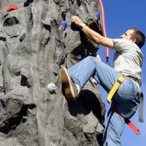 A man climbs an outdoor rock climbing wall on a sunny day.