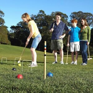 Four people are playing croquet on a grassy field under a clear blue sky.