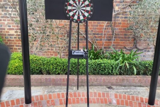 A freestanding dart board setup outdoors, with a scoreboard labeled "Home" and "Away" above it.