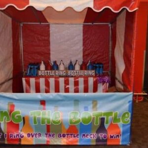 A ring toss game stall at a funfair with colorful bottles and a striped tent.