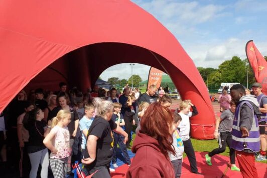 A crowd gathers under a large red inflatable event dome on a sunny day.