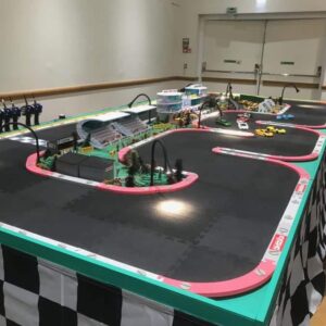 A model race track with remote-controlled cars and controllers on a checkered table.