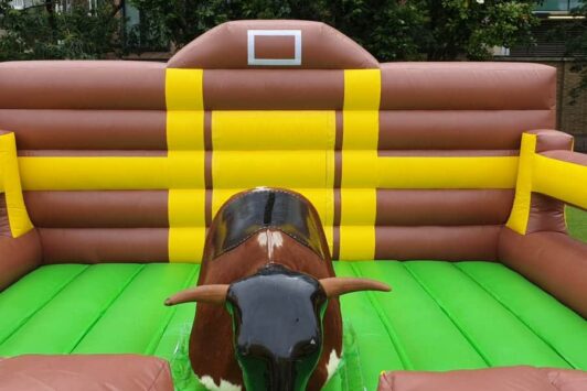 Inflatable rodeo bull ride on a green and brown padded mat outdoors.