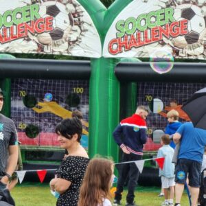 People gathered in front of inflatable soccer challenge games at an outdoor event.