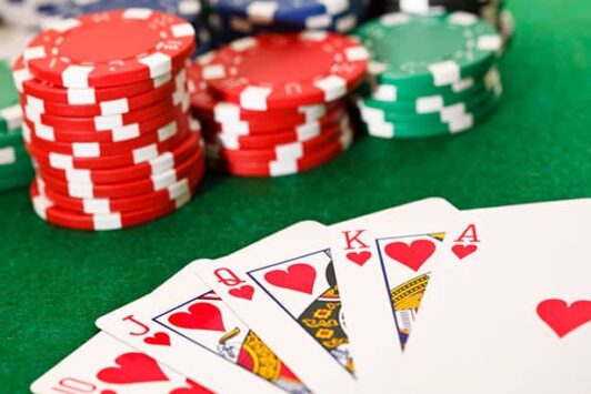 A royal flush in hearts with poker chips on a green casino table.