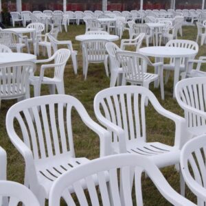 Rows of white plastic tables and chairs set up outdoors on grass.