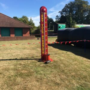 Red "Test Your Strength" carnival game stands on grass under a blue sky.