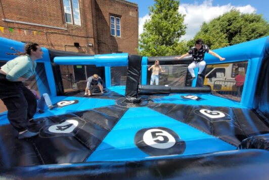 People playing on an inflatable wipeout simulator outdoors on a sunny day.