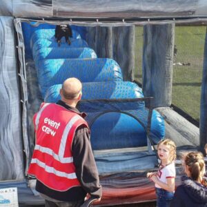 Children line up at an inflatable obstacle course with an event crew member supervising.